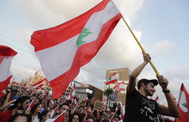 Lebanese demonstrators wave national flags on a highway linking Beirut to north Lebanon, in Zouk Mikael on October 19, 2019, a day after demonstrations swept through the eastern Mediterranean country in protest against dire economic conditions. - Thousands of protesters outraged by corruption and proposed tax hikes burned tyres and blocked major highways in Lebanon on Friday, prompting the premier to give his government partners three days to support a reform drive. (Photo by JOSEPH EID / AFP)