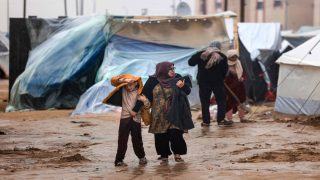 Palestinians walk under the rain at a camp for displaced people in Rafah, in the southern Gaza Strip where most civilians have taken refuge, on December 13, 2023, as battles continue between Israel and the Palestinian militant group Hamas. Israel came under pressure on December 13 from its allies over its war in Gaza, with key backer the United States criticising its bombing in response to the October 7 attacks as "indiscriminate". (Photo by MAHMUD HAMS / AFP)